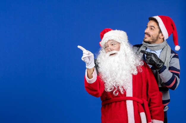 Vista frontal de santa claus con joven en la pared azul