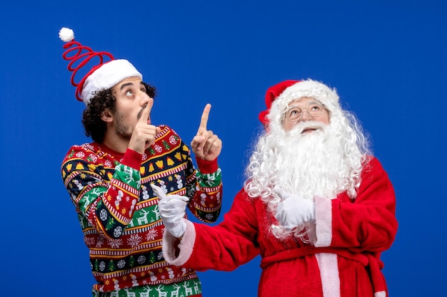 Vista frontal de santa claus con joven en la pared azul