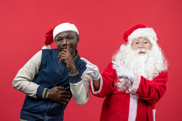 Vista frontal de santa claus con joven en una pared roja