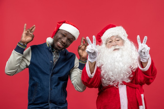 Vista frontal de santa claus con joven en la pared roja