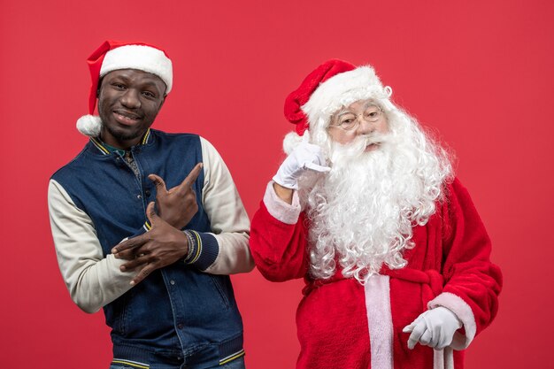 Vista frontal de santa claus con joven en la pared roja