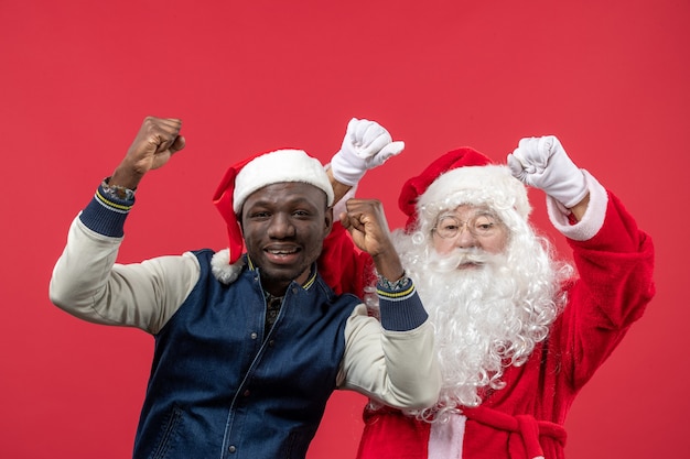 Vista frontal de santa claus con joven en la pared roja