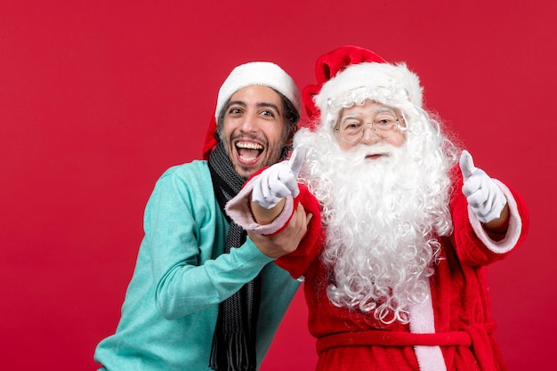 Vista frontal de santa claus con joven posando en la pared roja