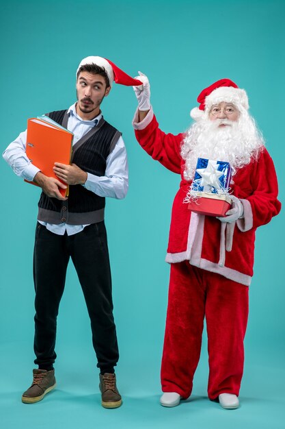 Vista frontal de santa claus con joven y presenta en pared azul