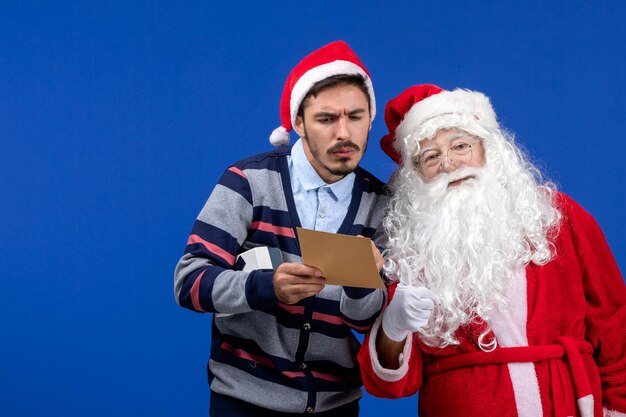 Vista frontal de santa claus con joven que lee una carta en la pared azul