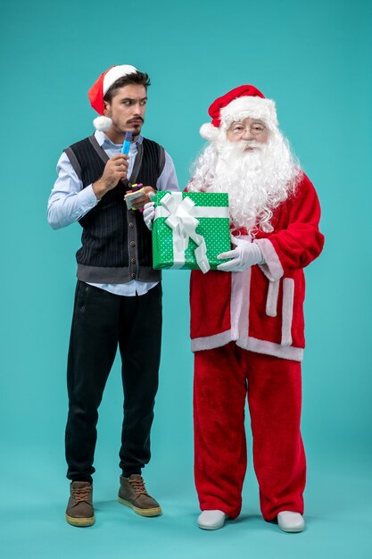 Vista frontal de santa claus con joven y regalo de vacaciones en la pared azul