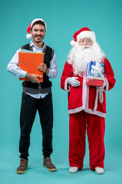 Vista frontal de santa claus con joven y regalos navideños en la pared azul