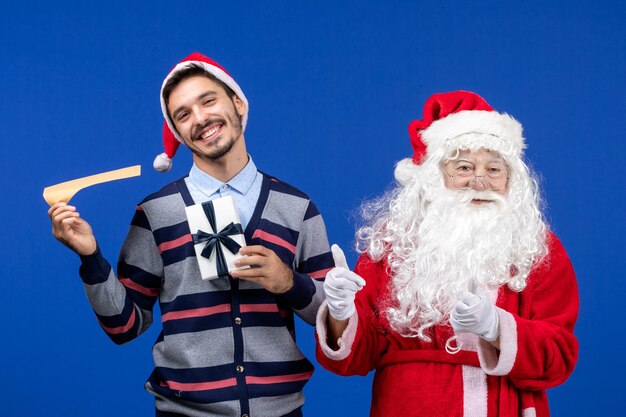 Vista frontal de santa claus con joven sosteniendo carta y presente en la pared azul