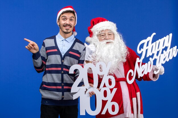 Vista frontal de santa claus con joven sosteniendo feliz año nuevo y escrito por ciento en pared azul