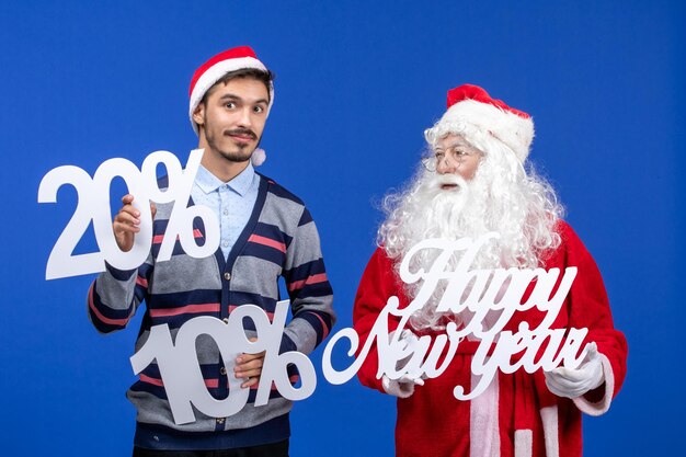 Vista frontal de santa claus con joven sosteniendo feliz año nuevo y números escritos en la pared azul