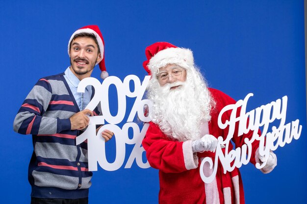 Vista frontal de santa claus con joven sosteniendo feliz año nuevo y números escritos en la pared azul