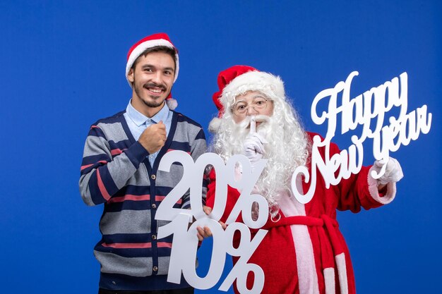 Vista frontal de santa claus con joven sosteniendo Feliz año nuevo y porcentaje de escrituras en pared azul