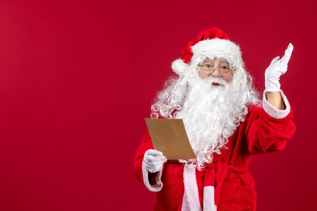 Vista frontal santa claus leyendo la carta de niño en rojo presenta emoción de vacaciones de navidad