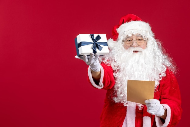 Vista frontal santa claus leyendo la carta de un niño y sosteniendo el presente en el piso rojo emoción regalo vacaciones de navidad