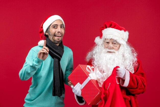 Vista frontal de santa claus con macho sacando el presente de la bolsa en el color rojo de vacaciones de emoción de Navidad