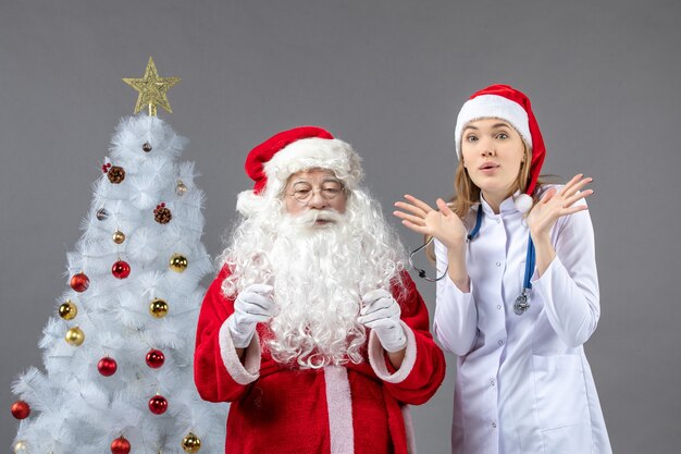 Vista frontal de santa claus con médico joven en la pared gris