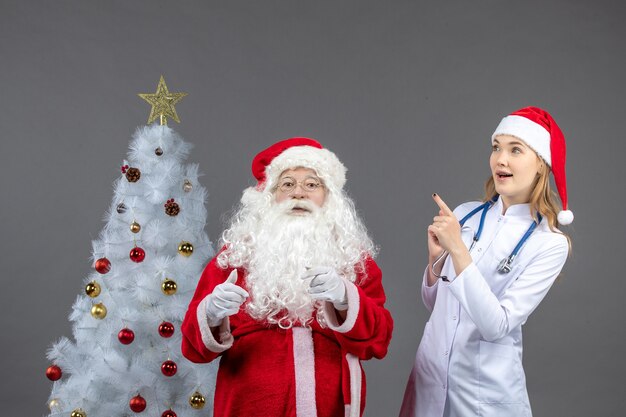 Vista frontal de santa claus con médico joven en la pared gris