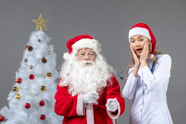 Vista frontal de santa claus con médico joven en la pared gris