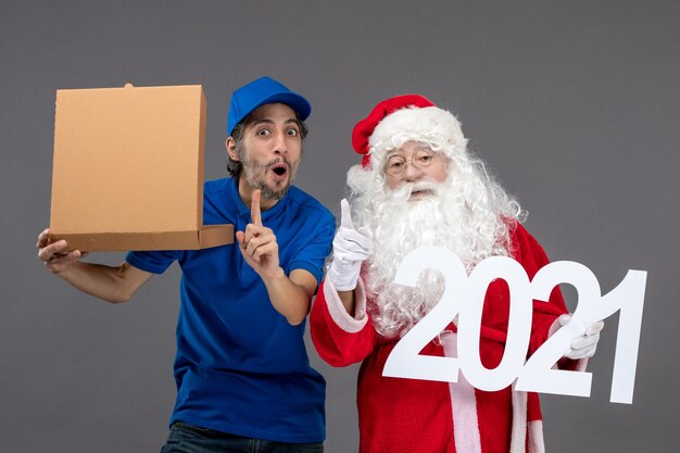 Vista frontal de santa claus con mensajero masculino con caja de comida y en la pared gris