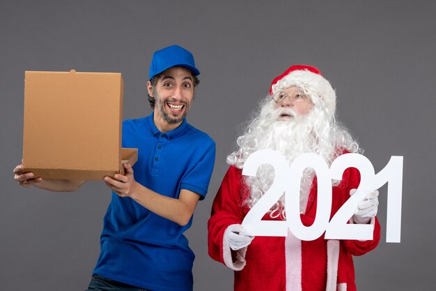 Vista frontal de santa claus con mensajero masculino con caja de comida y en la pared gris