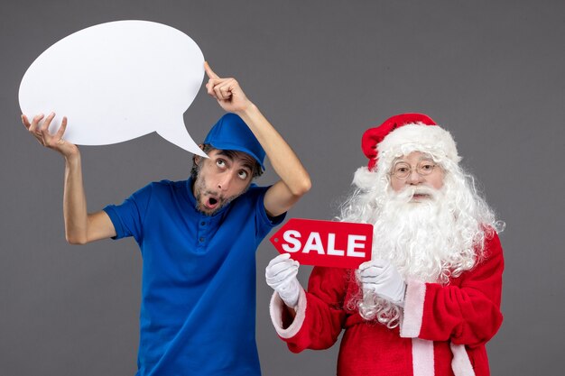 Vista frontal de santa claus con mensajero masculino con cartel blanco y pancarta de venta en la pared gris