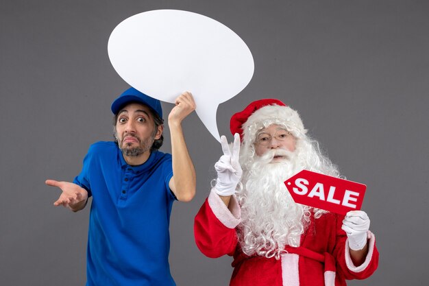 Vista frontal de santa claus con mensajero masculino con cartel blanco y pancarta de venta en la pared gris