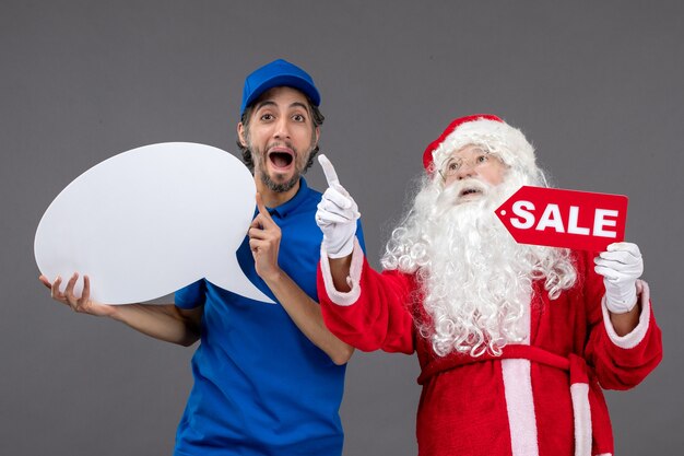 Vista frontal de santa claus con mensajero masculino con cartel blanco y pancarta de venta en la pared gris