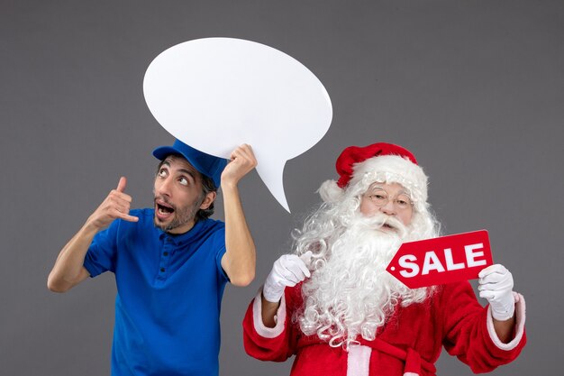 Vista frontal de santa claus con mensajero masculino con cartel blanco y pancarta de venta en la pared gris