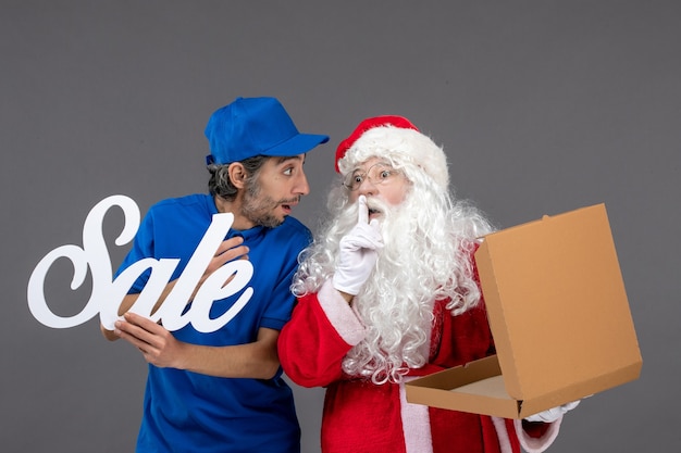 Vista frontal de santa claus con mensajero masculino con escritura de venta y caja de comida vacía en la pared gris