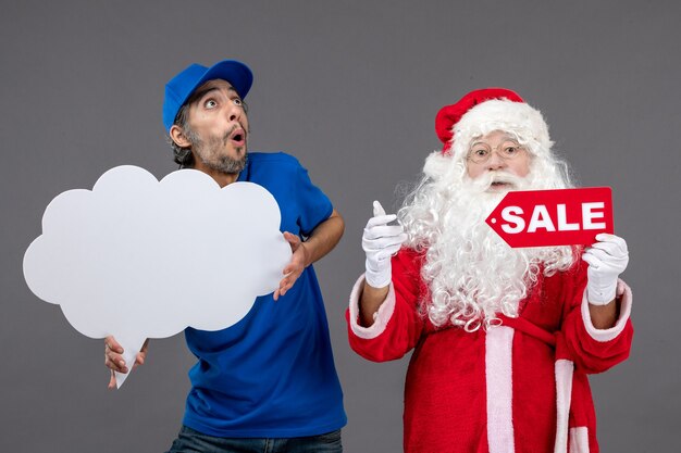 Vista frontal de santa claus con mensajero masculino con escritura de venta y signo de nube en pared gris