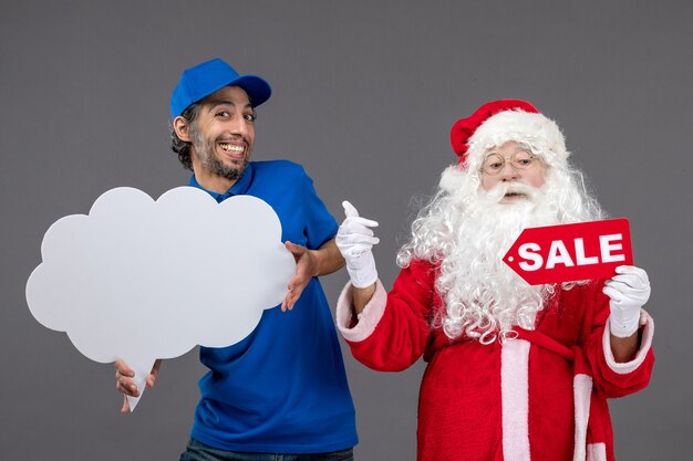 Vista frontal de santa claus con mensajero masculino con escritura de venta y signo de nube en pared gris