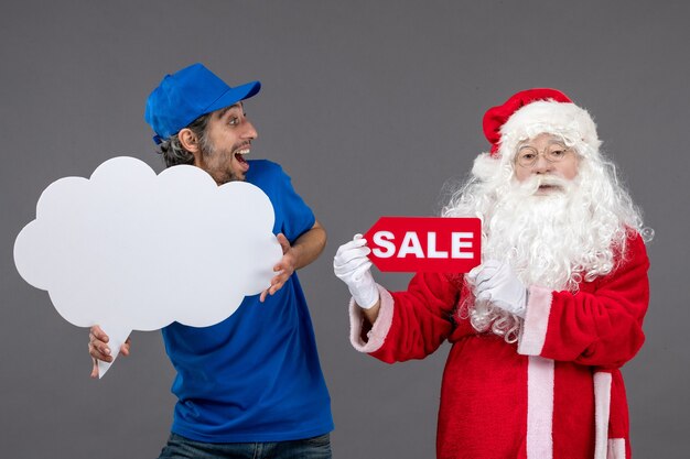 Vista frontal de santa claus con mensajero masculino con escritura de venta y signo de nube en pared gris