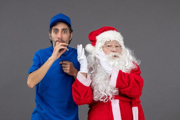 Vista frontal de santa claus con mensajero masculino joven sobre fondo gris