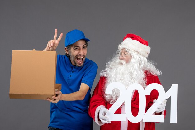 Vista frontal de santa claus con mensajero masculino sosteniendo caja de comida y escribiendo en la pared gris