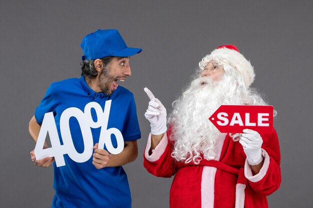 Vista frontal de santa claus con mensajero masculino sosteniendo pancartas de venta en la pared gris