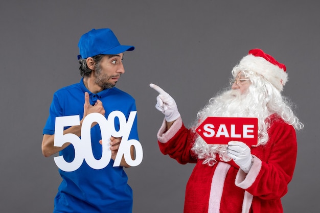 Vista frontal de santa claus con mensajero masculino sosteniendo pancartas de venta en la pared gris