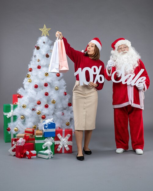 Vista frontal de santa claus con mujer joven sosteniendo y escritos de venta sobre el fondo gris