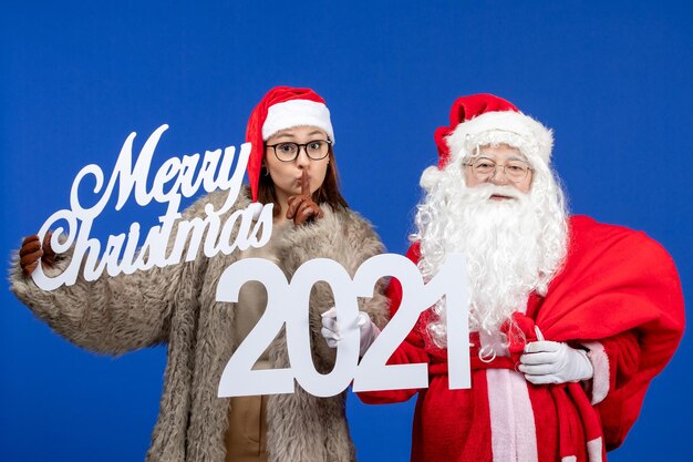 Vista frontal de santa claus con mujer joven sosteniendo feliz navidad y escritos en color azul emoción vacaciones navidad año nuevo