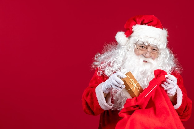 Vista frontal de santa claus con presente de una bolsa llena de regalos para niños en año nuevo de emociones rojas