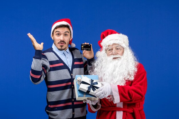 Vista frontal de santa claus con regalos y hombre joven con tarjeta bancaria en azul emoción de Navidad nueva