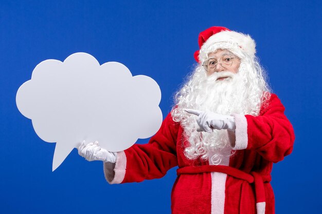 Vista frontal de santa claus sosteniendo un gran cartel en forma de nube blanca en el escritorio azul color nieve vacaciones navidad