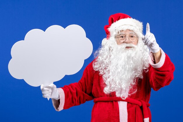 Vista frontal de santa claus sosteniendo un gran cartel en forma de nube en el escritorio azul color nieve navidad