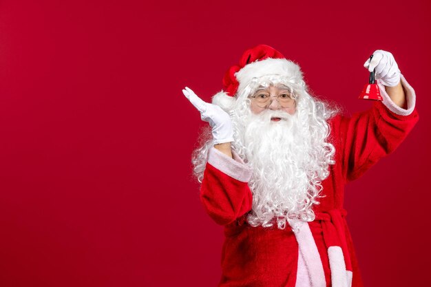 Vista frontal de santa claus sosteniendo una pequeña campana en la emoción de regalo rojo vacaciones de año nuevo de navidad