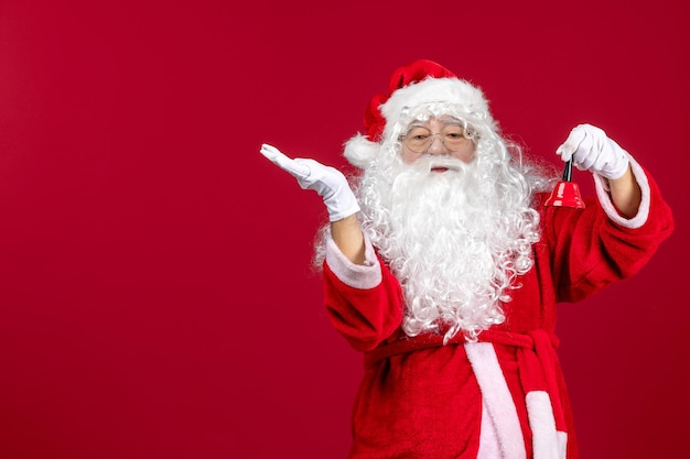 Foto gratuita vista frontal de santa claus sosteniendo una pequeña campana en un escritorio rojo emoción de regalo vacaciones de navidad año nuevo