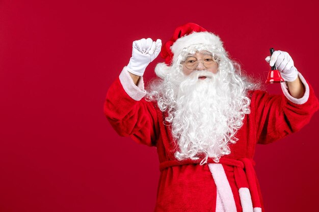 Vista frontal de santa claus sosteniendo la pequeña campana en el escritorio rojo navidad año nuevo emoción vacaciones