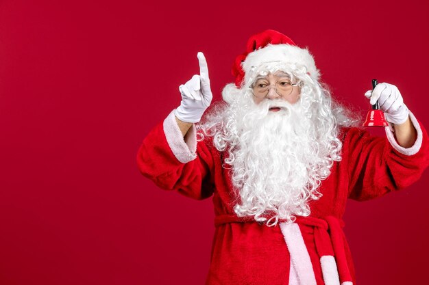 Vista frontal de santa claus sosteniendo una pequeña campana en el piso rojo navidad año nuevo emoción vacaciones