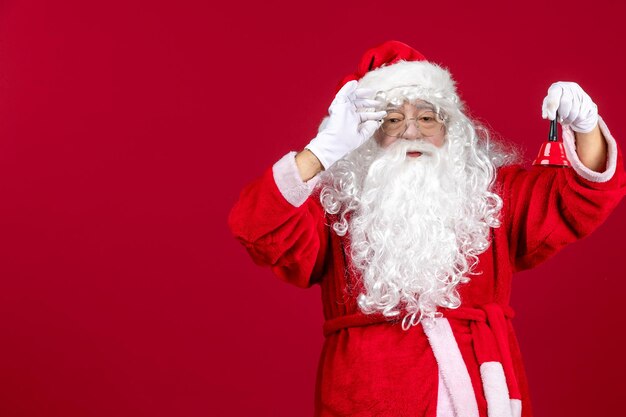 Vista frontal de santa claus sosteniendo la pequeña campana en regalo rojo vacaciones de navidad año nuevo emoción