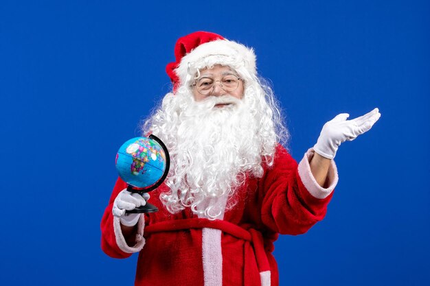 Vista frontal de santa claus sosteniendo un pequeño globo terráqueo en azul año nuevo colores vacaciones de navidad