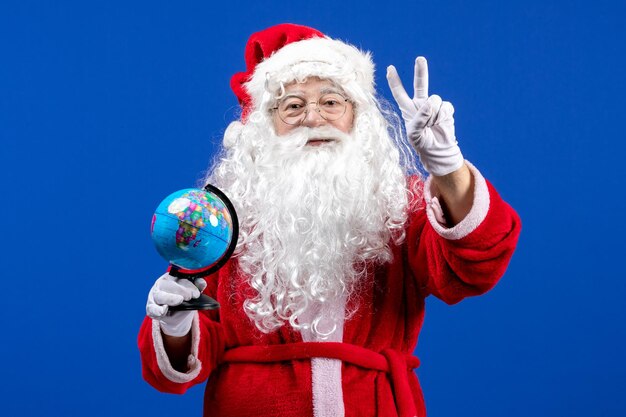 Vista frontal de santa claus sosteniendo un pequeño globo terráqueo en las vacaciones de navidad de color azul año nuevo