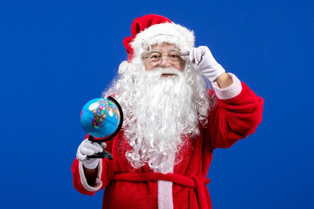 Vista frontal de santa claus sosteniendo un pequeño globo terráqueo en las vacaciones de navidad de color azul año nuevo